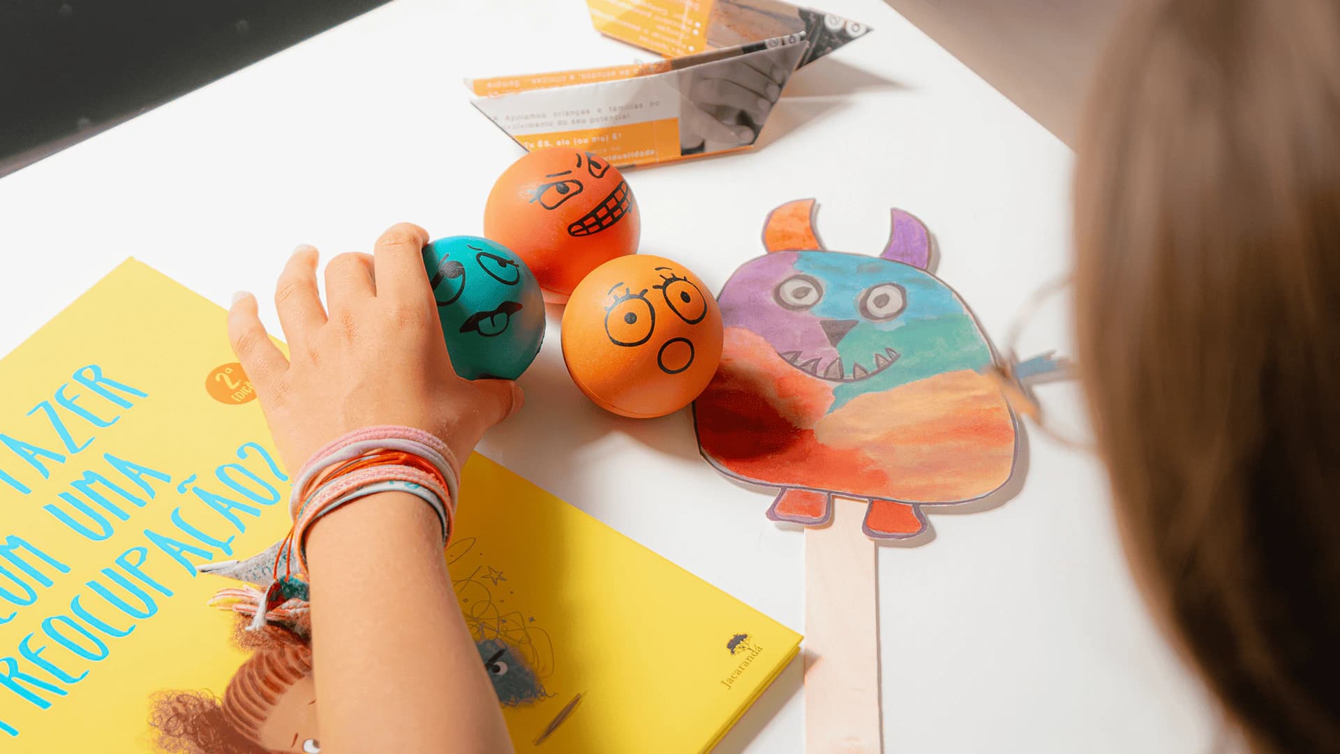 Criança a explorar bolas com expressões e um desenho numa atividade sobre emoções