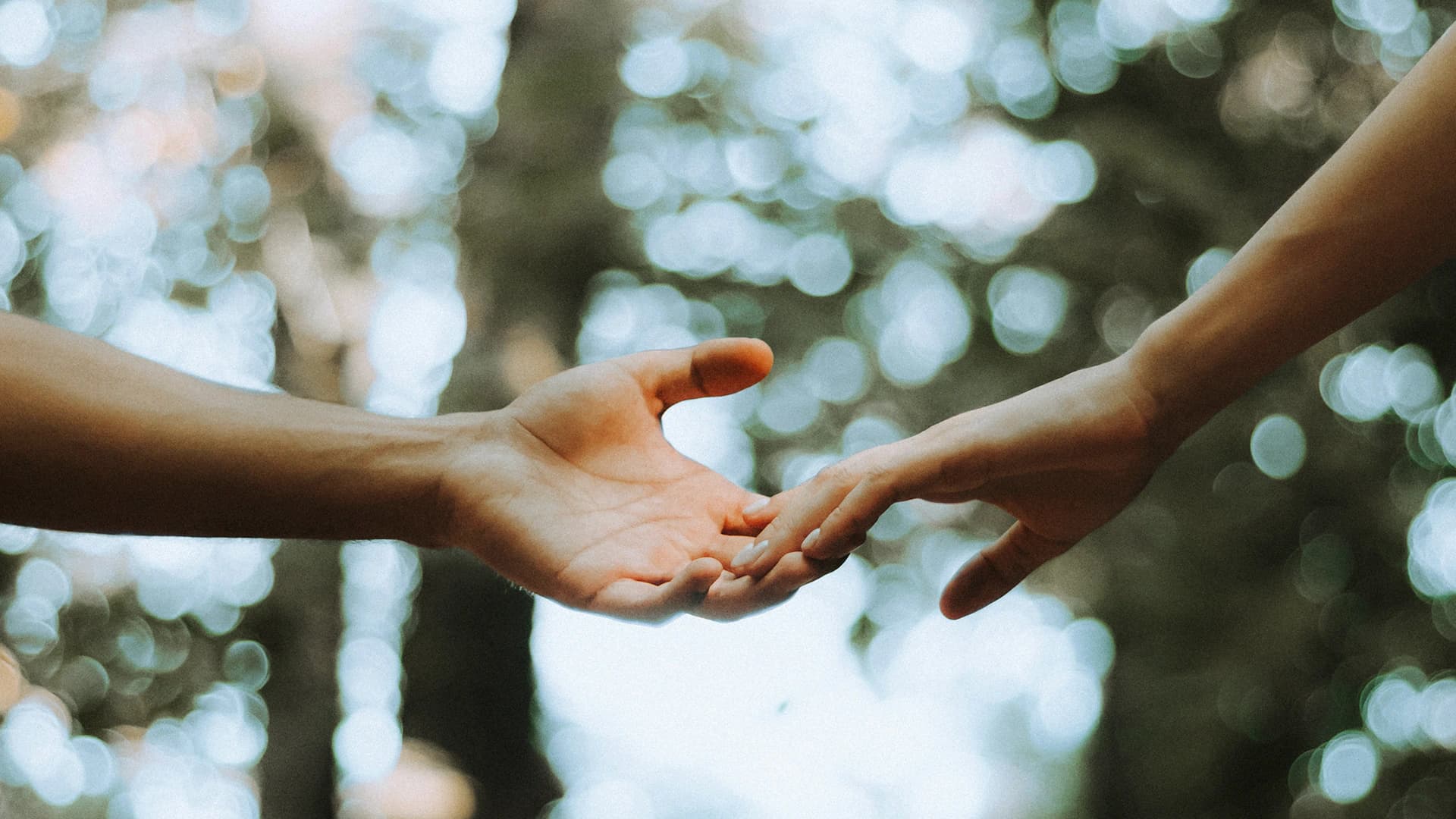 Duas pessoas estendem as mãos uma à outra ao ar livre